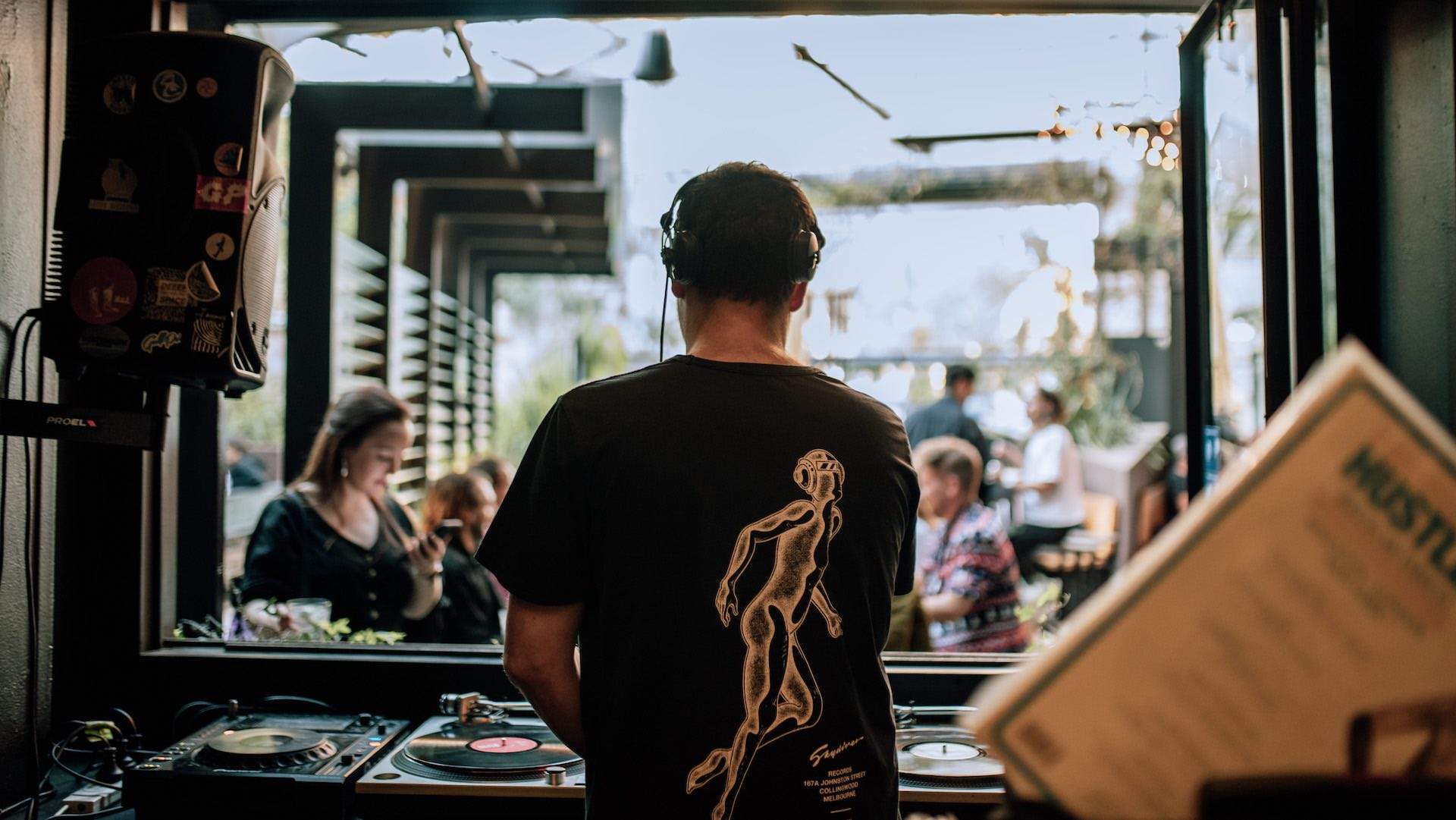 Focus on DJ with casual audience in background at Howler, Melbourne.