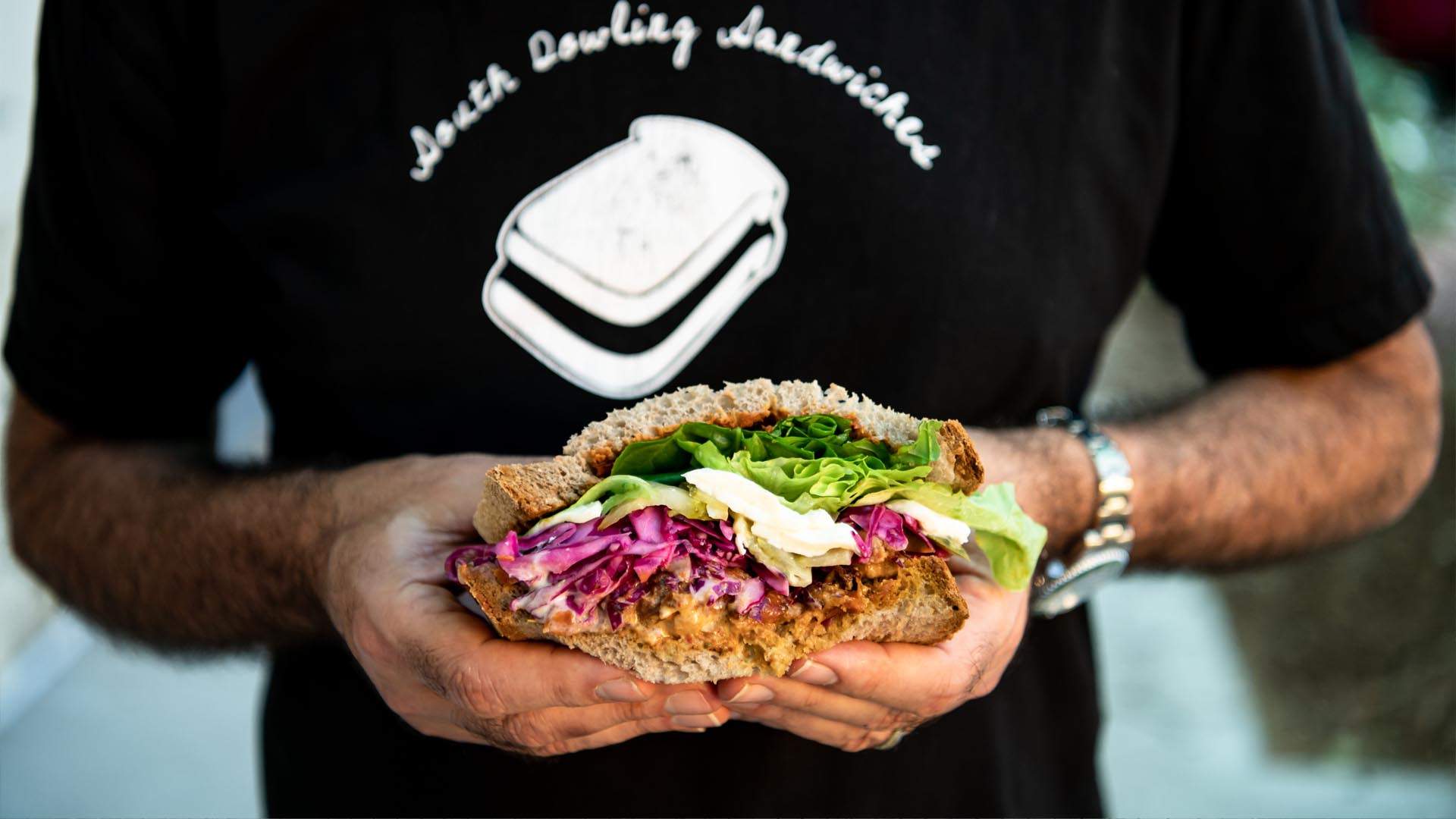 A person holding a loaded salad sandwich from South Dowling Sandwiches — one of the best sandwich shops in Sydney.