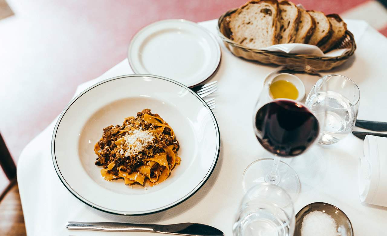 a table with pasta and red wine at Trattoria Emilia