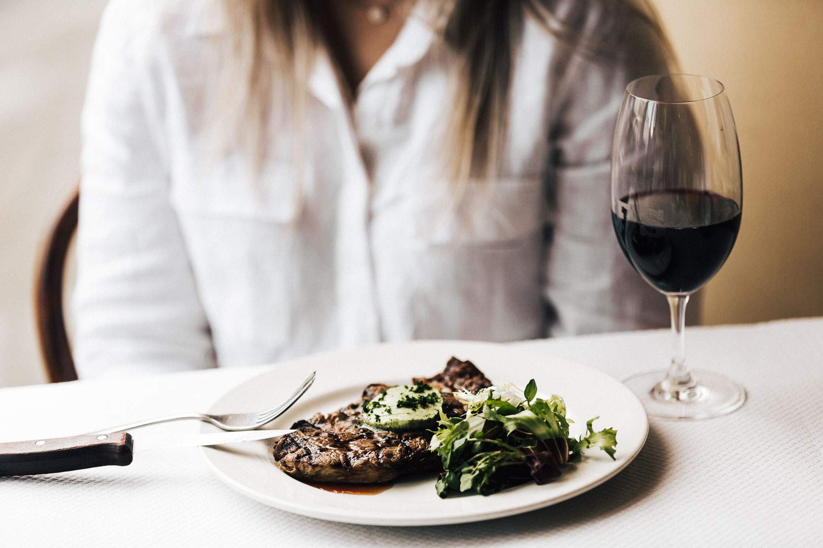 A woman sitting in front of steaka nd wine at France-soir - home to some of the best steaks in Melbourne