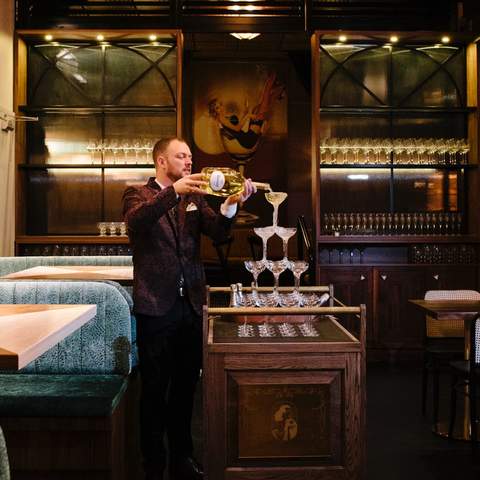 A man pouring Champagne on a tower of champagne glasses at Nick and Nora's - one of the best bars in Sydney - paramatta