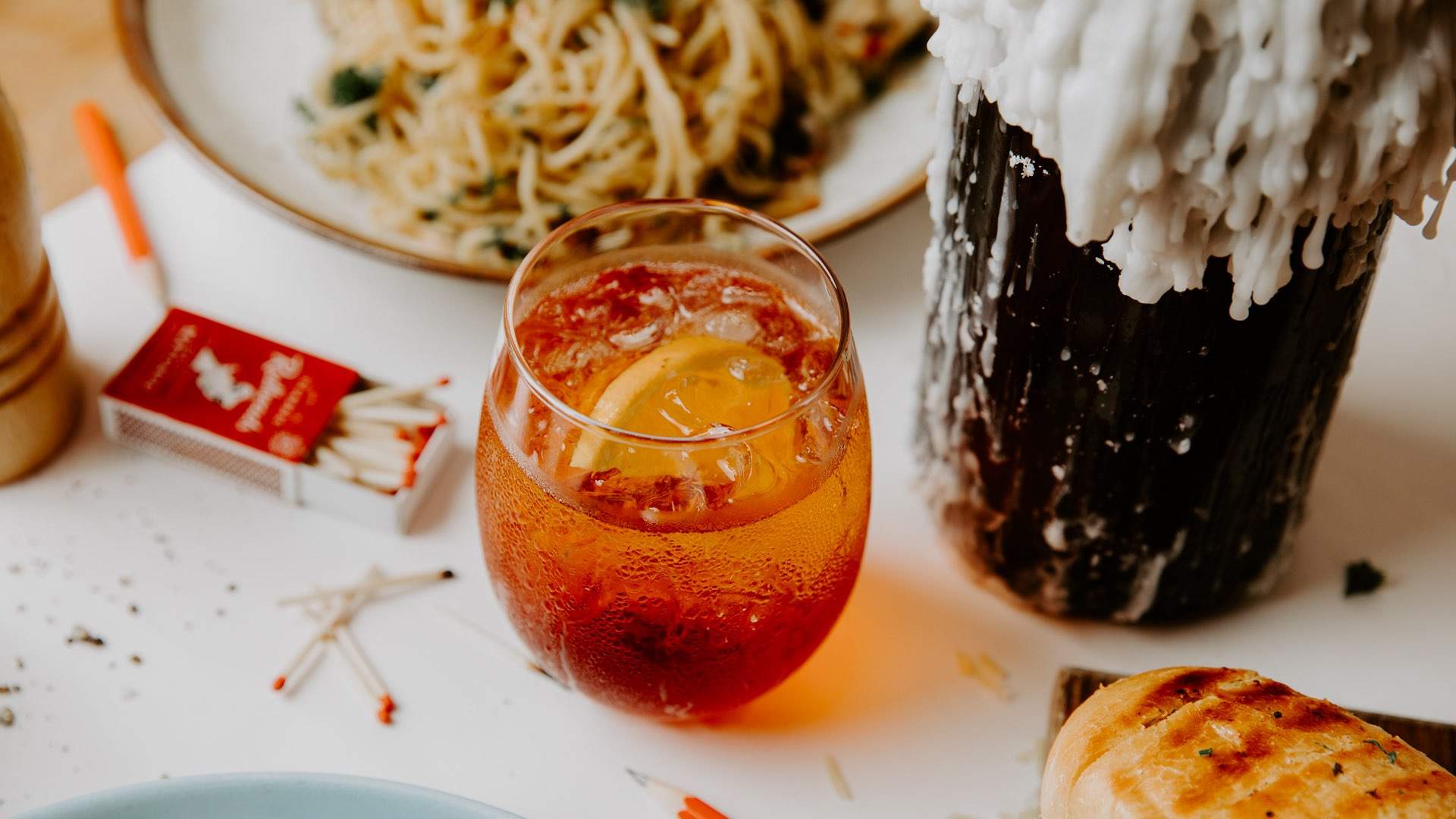 a negroni on a table with candles, matches and a bowl of pasta at Good Times in Fitzroy