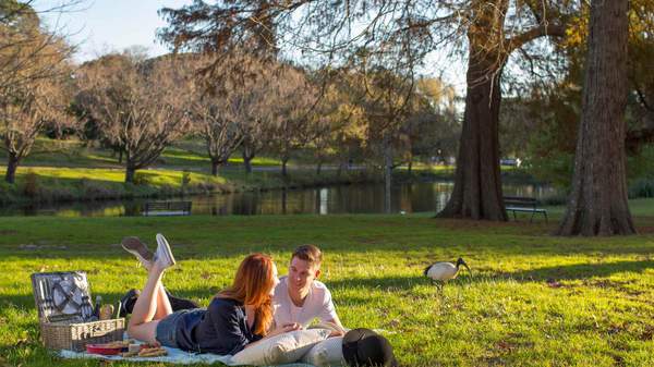 couple in Centennial Parklands laying on a picnic blanket with pond in the background