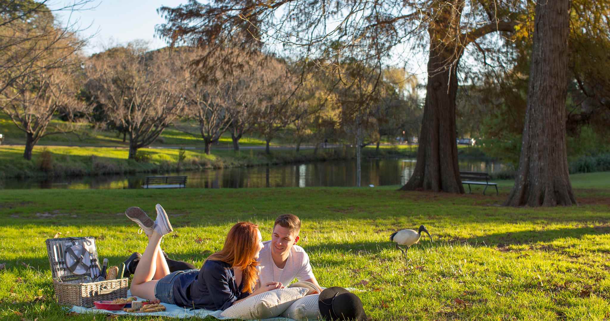 couple in Centennial Parklands laying on a picnic blanket with pond in the background