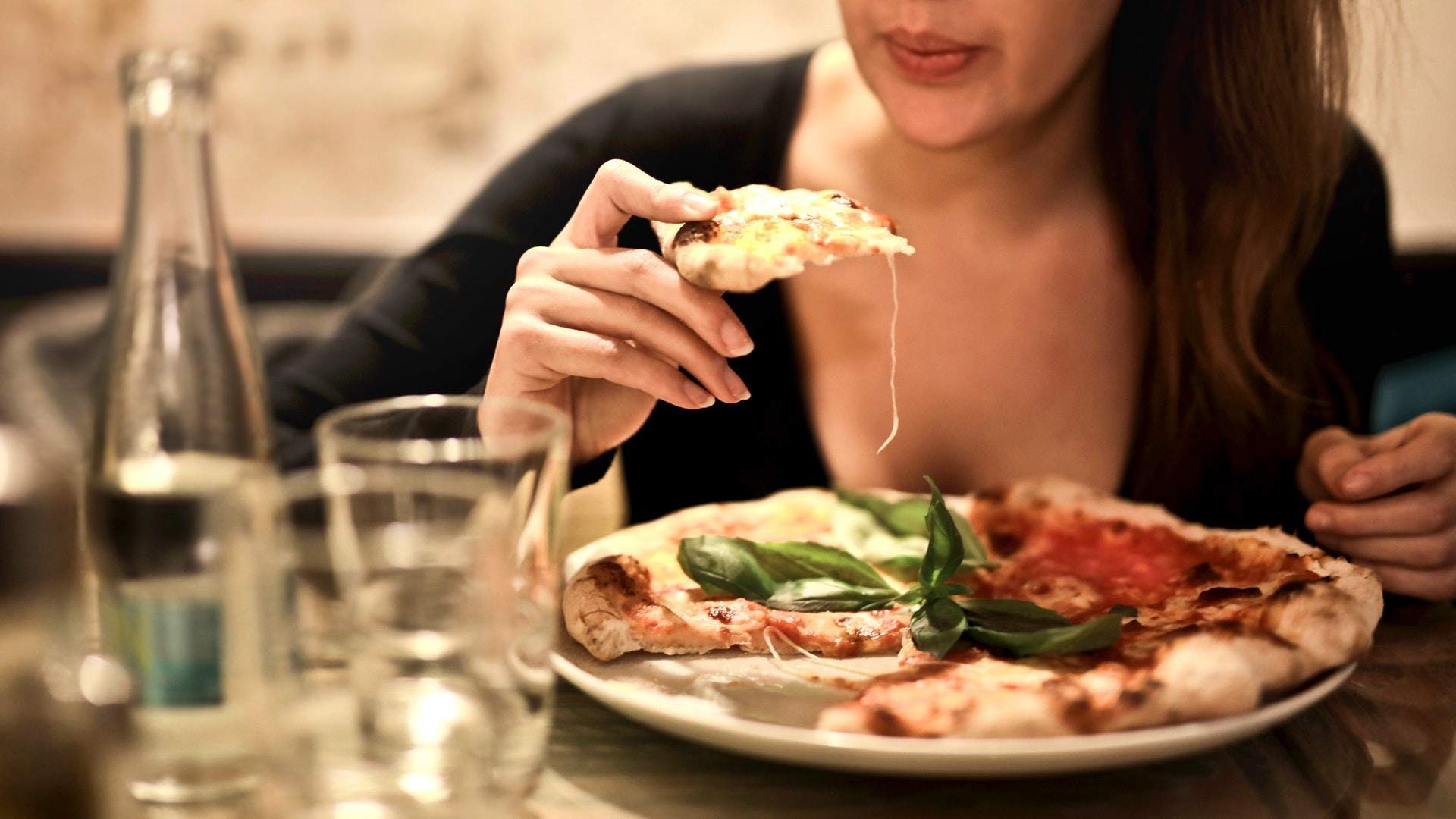 Woman holds sliced pizza with water on the table