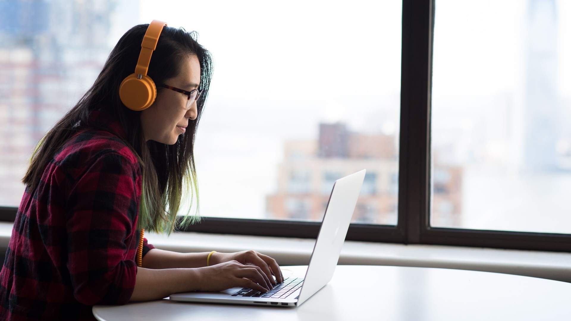 Woman with orange headphones using a laptop in a high-rise office