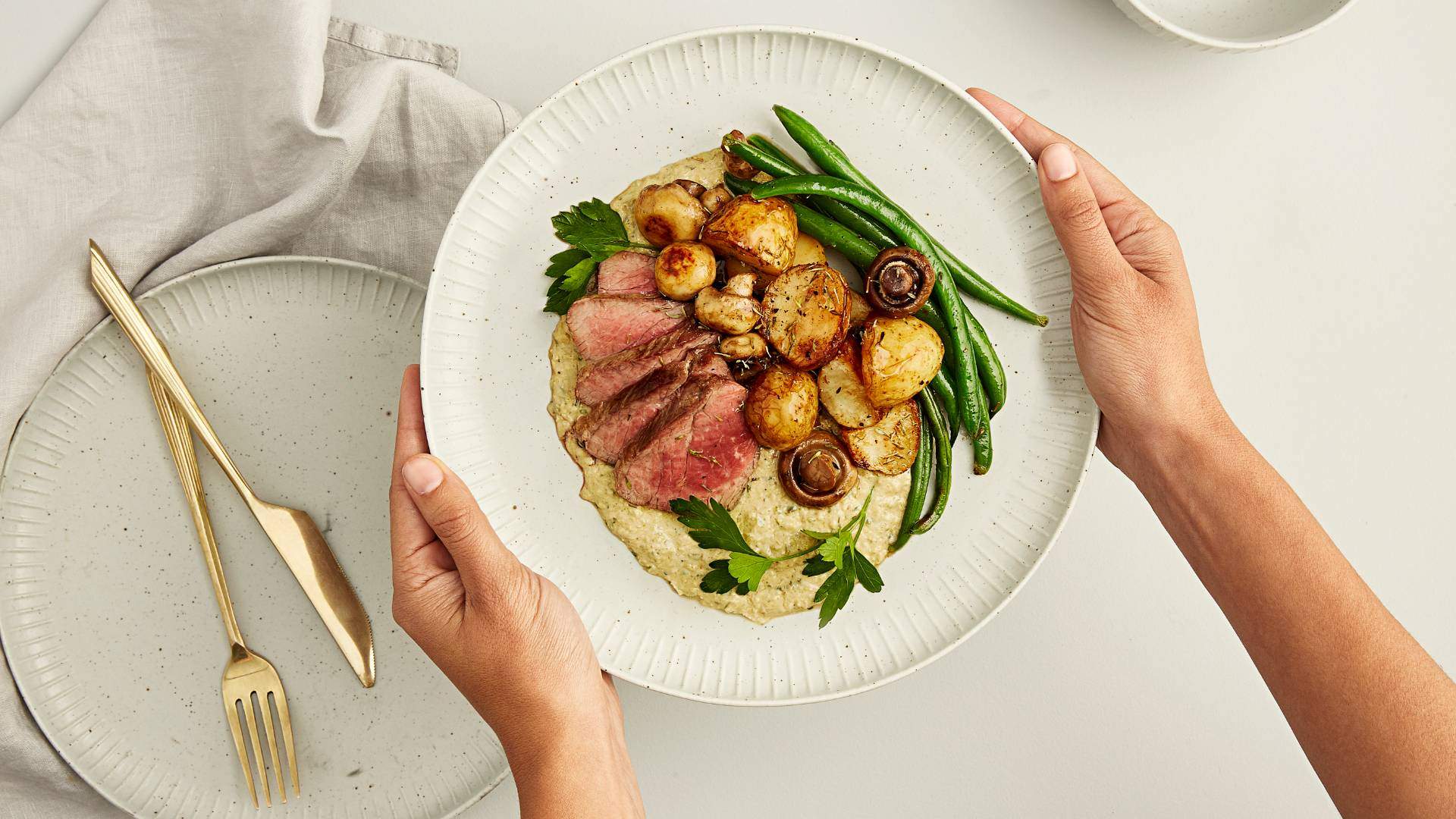 Person holding a plate of beef, potatoes and beans