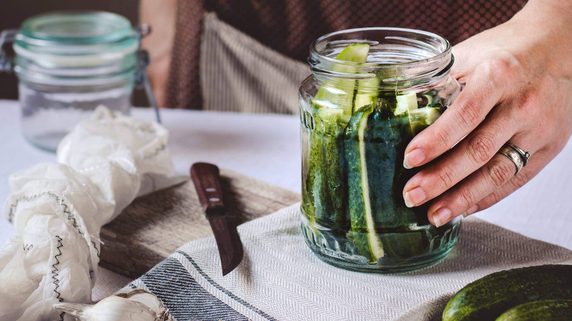 Person holding a glass jar of cucumbers ready to pickle