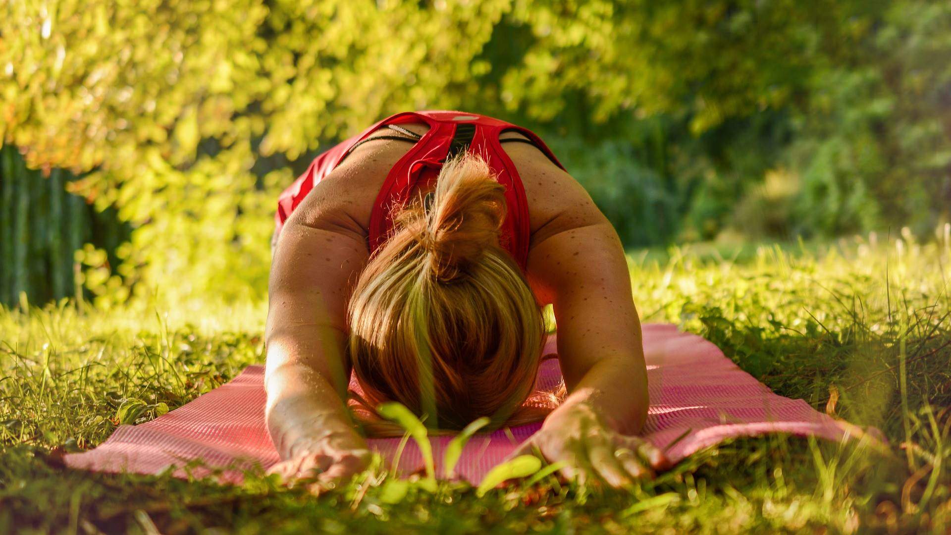 Woman in child's pose on a pink mat on the grass