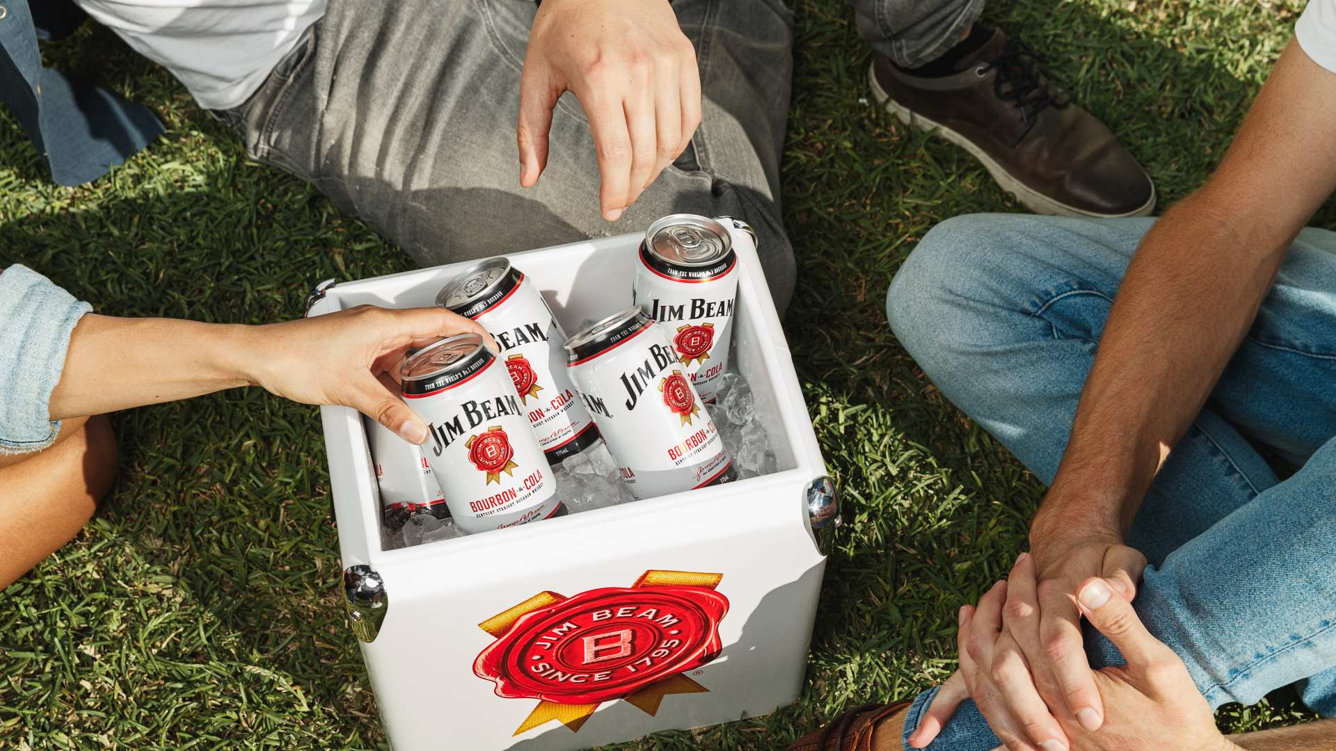 Three people sitting around an esky of Jim Beam premixers