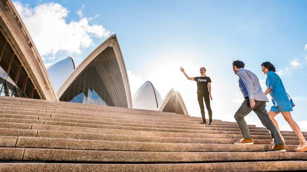Two people walking up the steps of Sydney Opera House with a tour guide