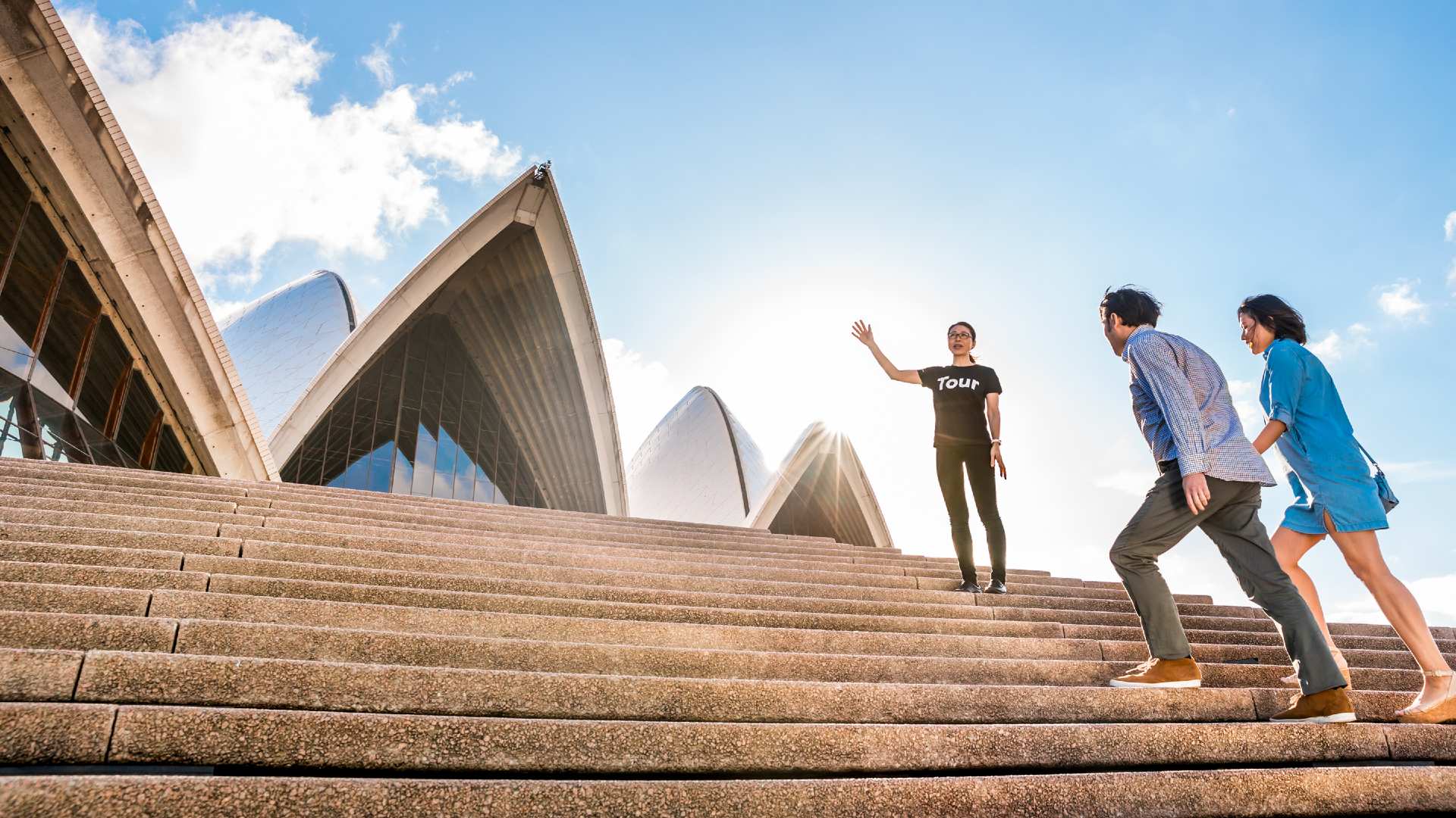 Two people walking up the steps of Sydney Opera House with a tour guide