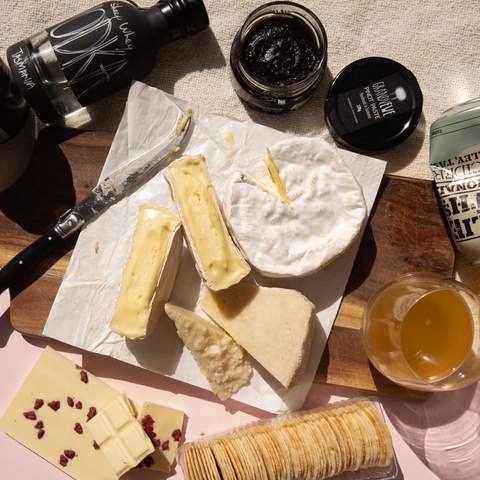 Cheese subscription gift including brie, pinot paste and cider on a wooden board