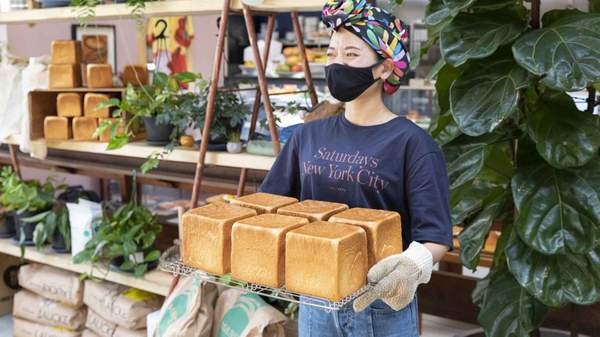 A person holding a tray of freshly made bread loaves. 