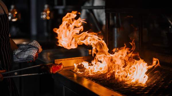 A chef cooking steak over wild flames on the grill at Embers at The Charming Squire in Brisbane.