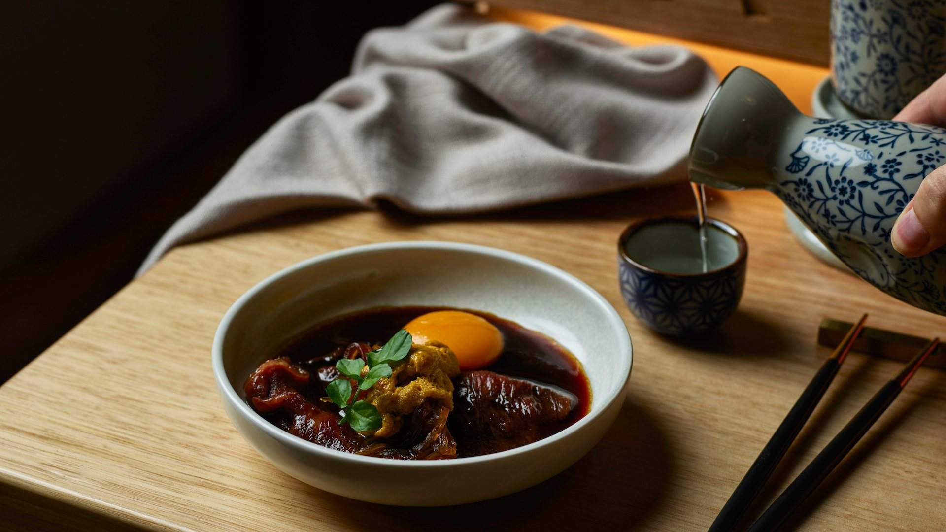 A dish and someone pouring sake at Bay Nine Omakase