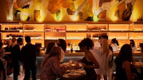 Two women dining at a high table with a back-lit bar behind them