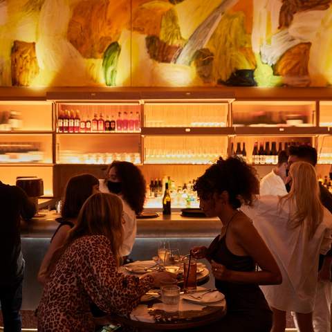 Two women dining at a high table with a back-lit bar behind them