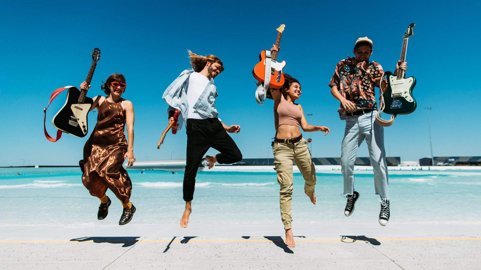 Four musicians jumping in front of a surf park