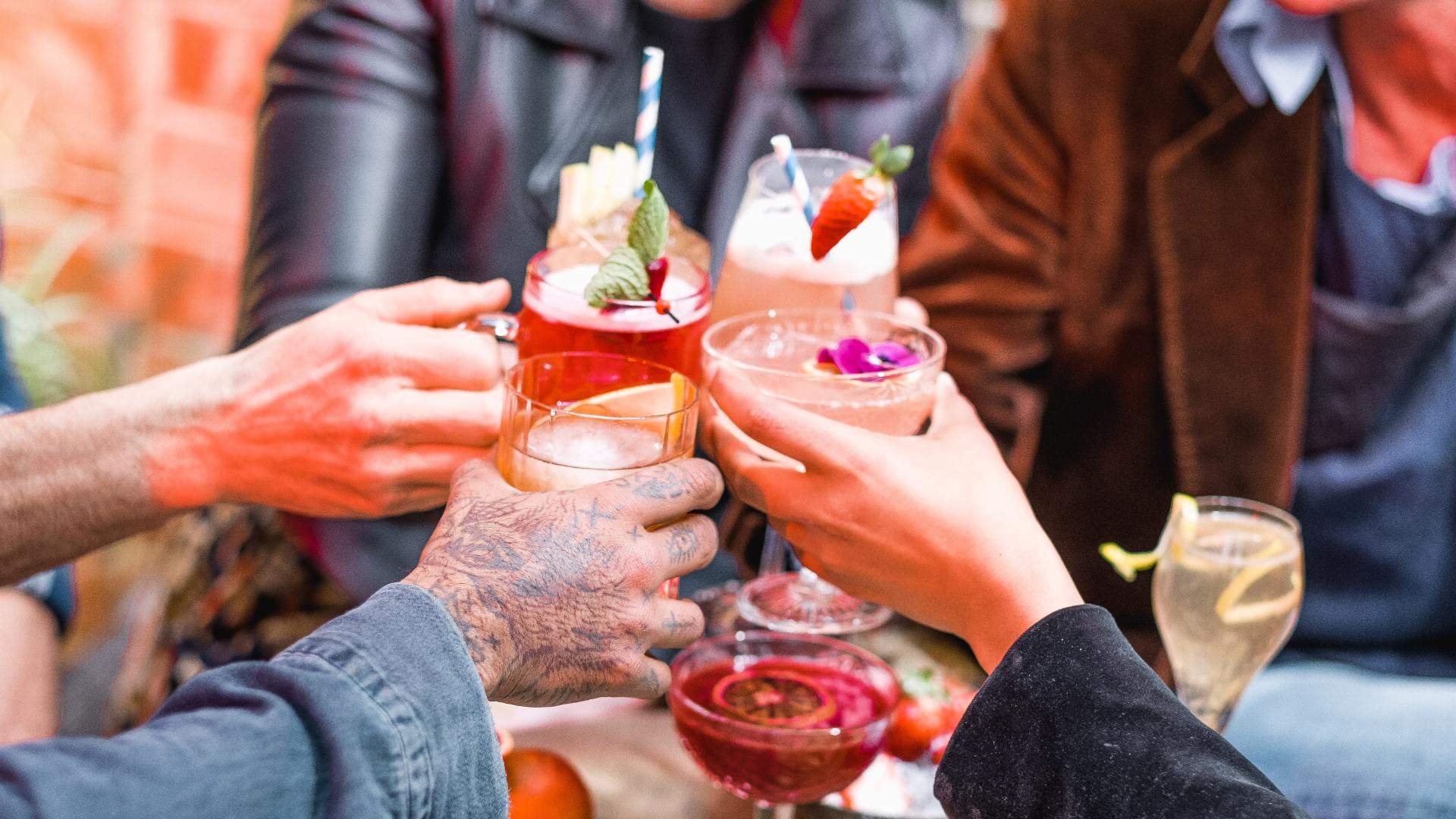 Four people cheersing with colourful cocktails