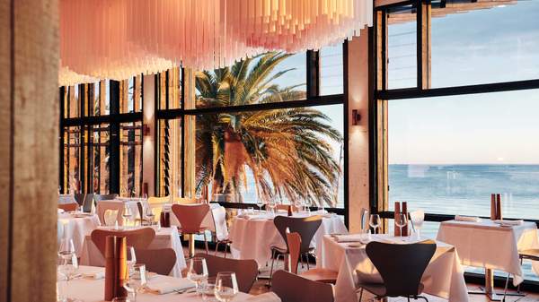 A shot of the dining area with a view through the glass windows which overlooks the water. 
