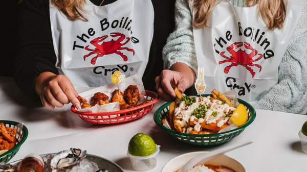 Two customers with seafood dishes wearing bibs that read 'The Boiling Crab'. 