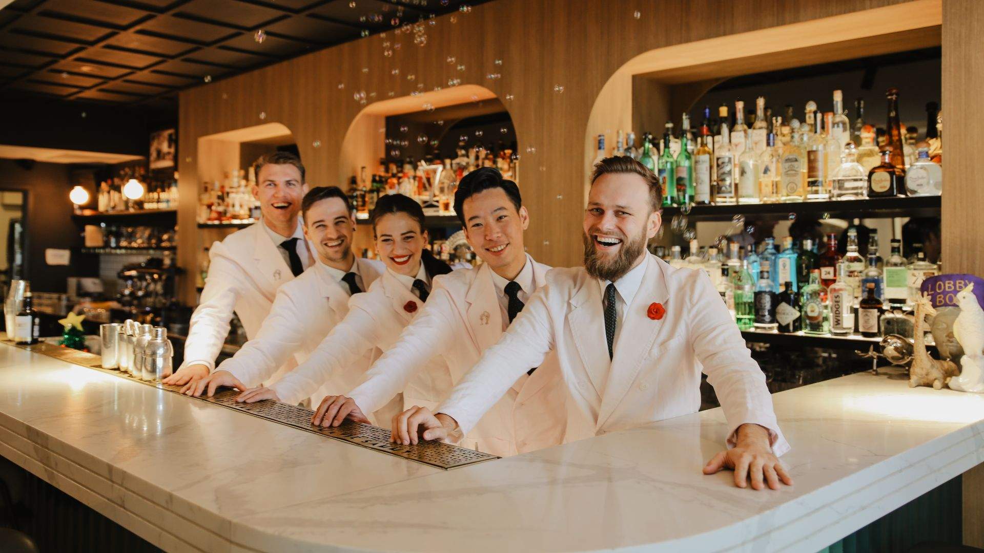 Five bartenders lining up at the bar, smiling in white suits at Maybe Sammy - one of the best bars in Sydney