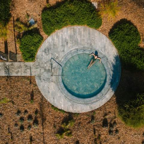 A woman relaxing in a large circular natural hot pool outside at Alba Thermal Pools - the best spa in Melbourne.