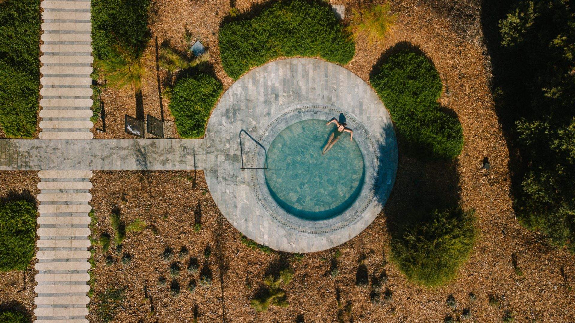 A woman relaxing in a large circular natural hot pool outside at Alba Thermal Pools - the best spa in Melbourne.
