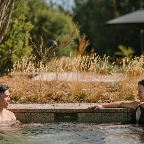 Two people relaxing in a large circular natural hot pool outside at Alba Thermal Pools - one of the best spas in Melbourne