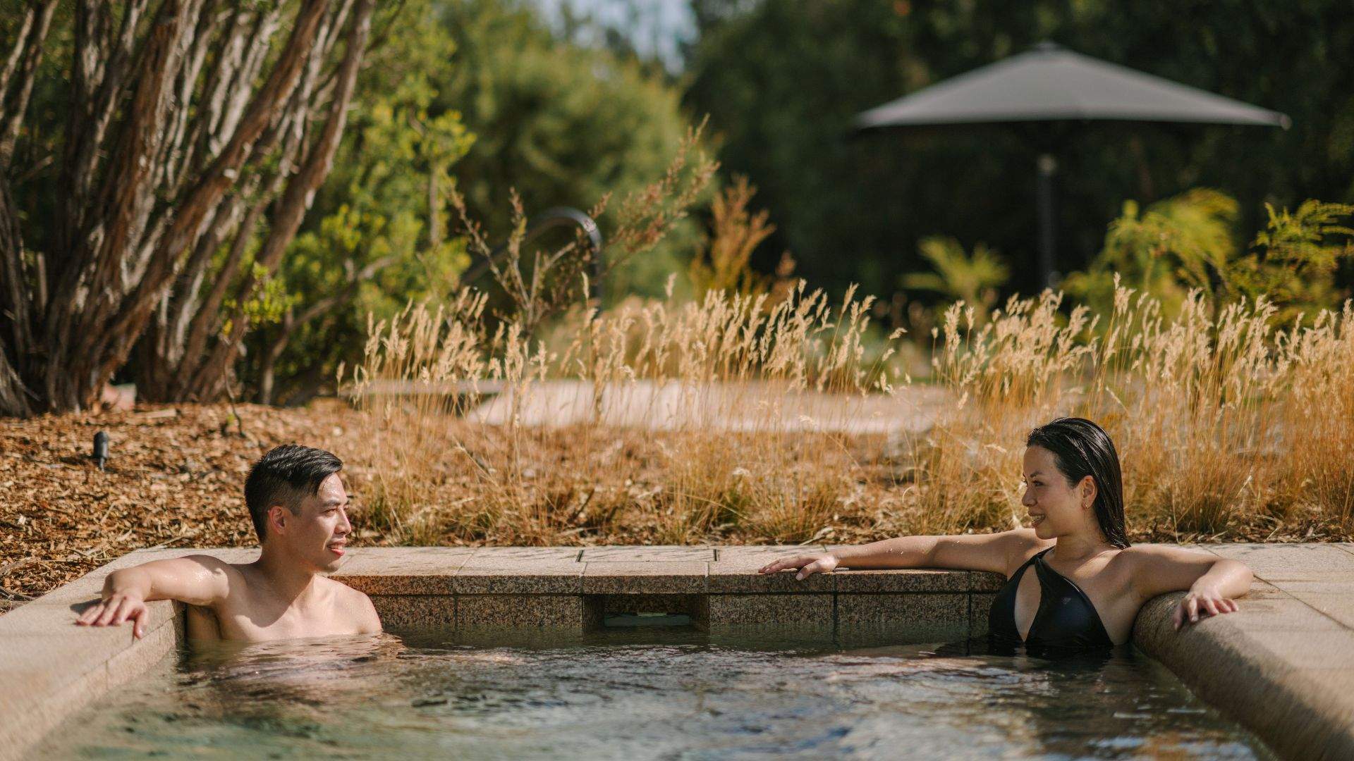 Two people relaxing in a large circular natural hot pool outside at Alba Thermal Pools - one of the best spas in Melbourne