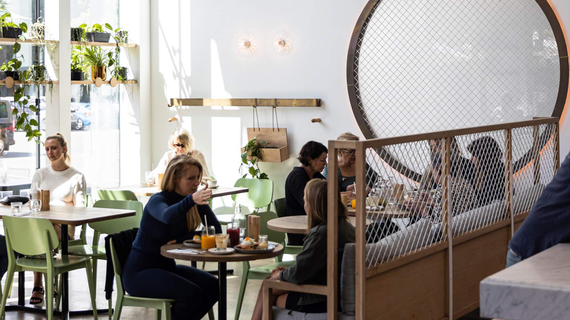 A sun-lit room filled with tables of men and women chatting over coffee, tea and food inside the Melbourne cafe called Kettle Black.