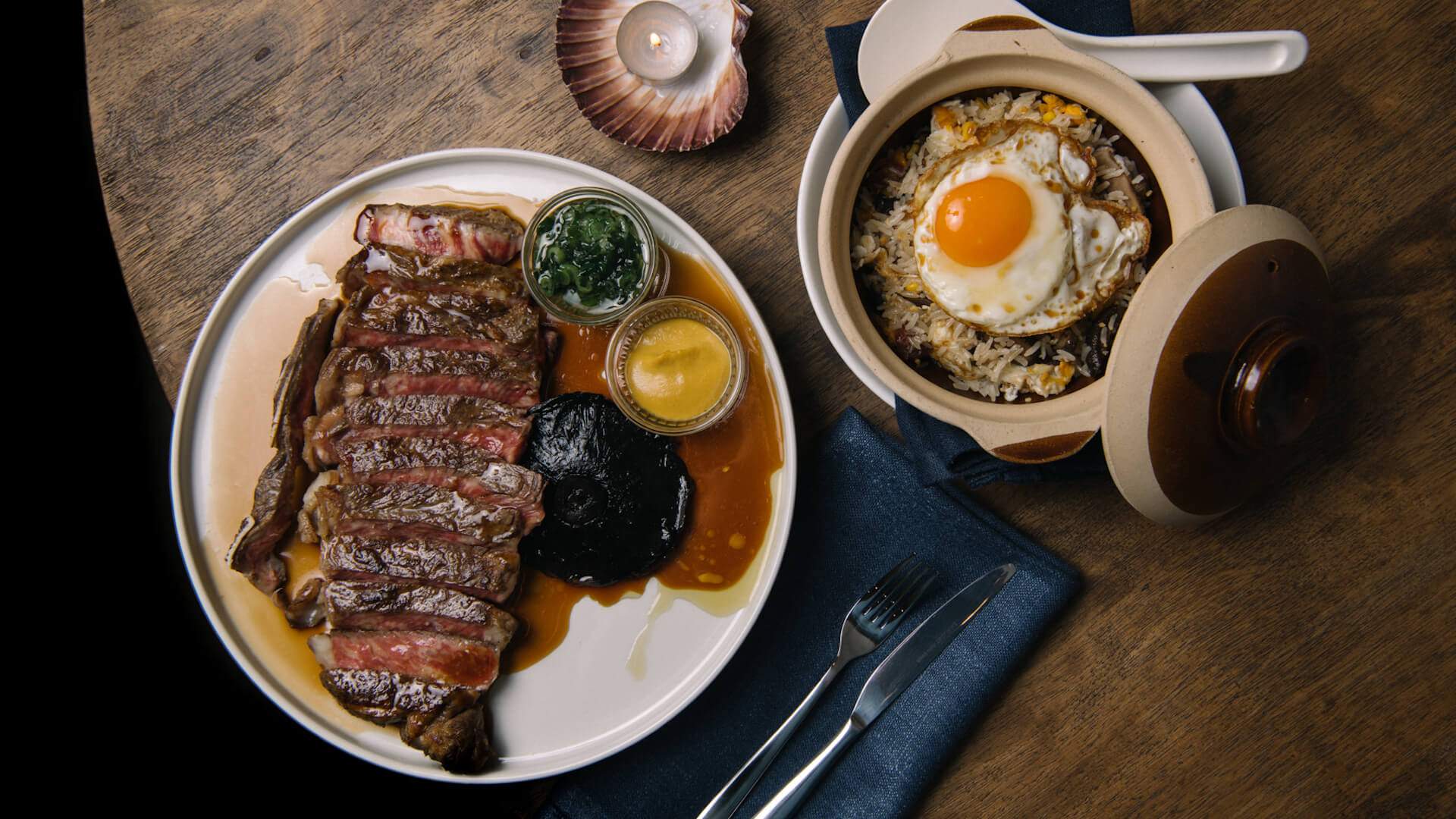 a wooden tabe with a large steak and pot of rice and a fried egg at S'more. home to one of the best steaks in Sydney