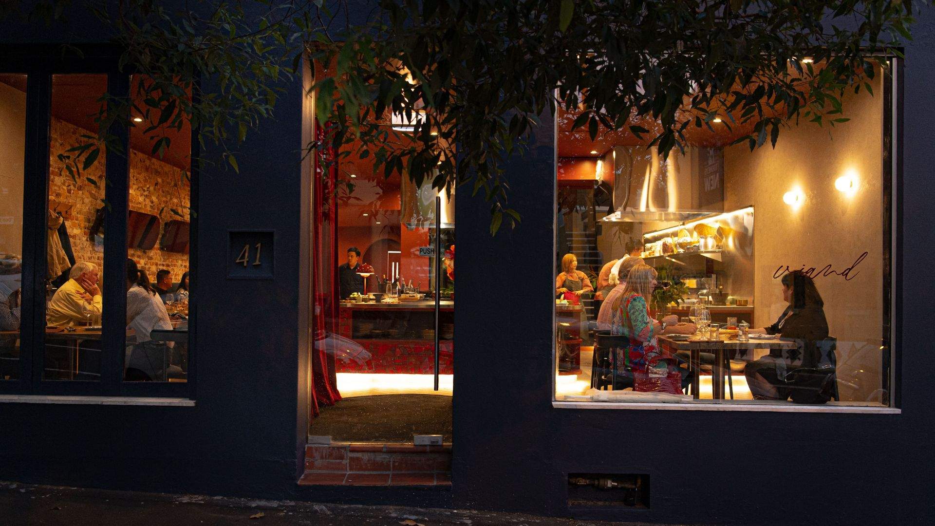 A view of Viand — one of the best thai restaurants in Sydney - from the street, looking through the windows at night