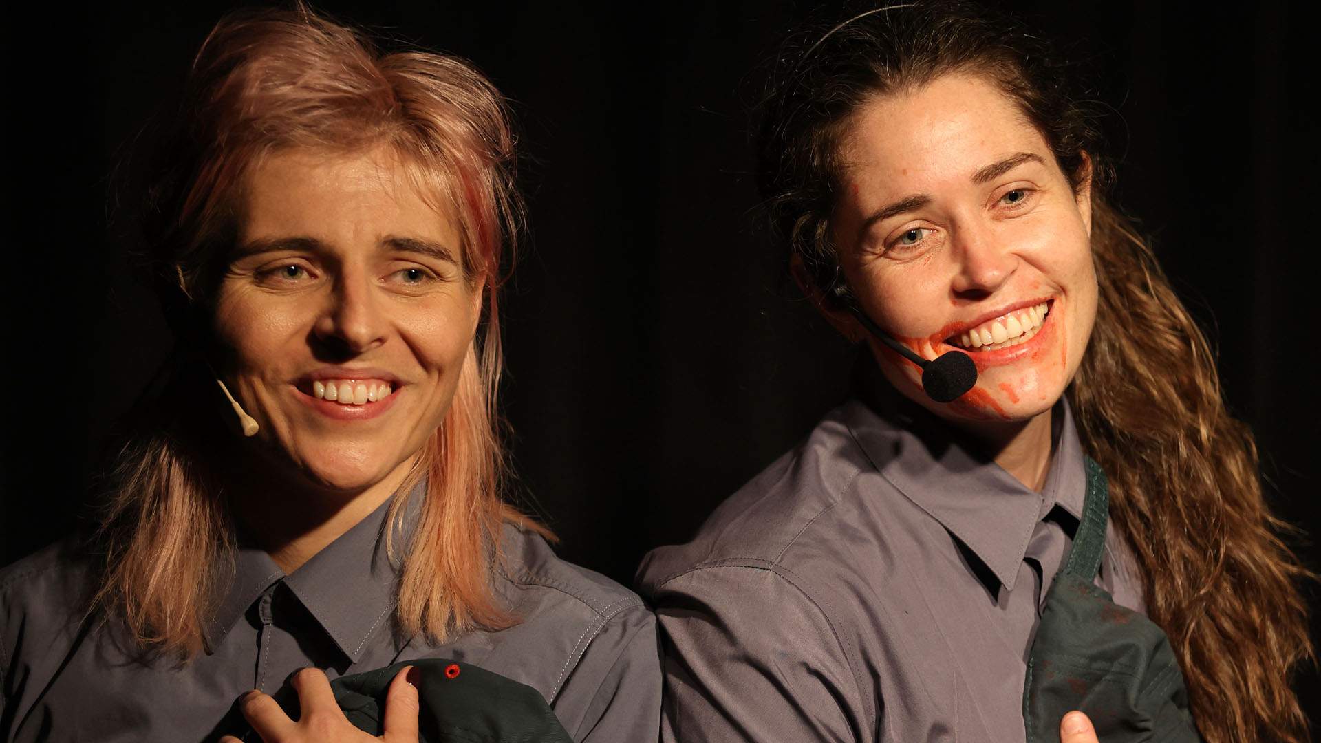 Two comedians in grey shirts and blood on their mouths holding Bunnings hats as part of the production 'Jazz, or a Bucket of Blood'