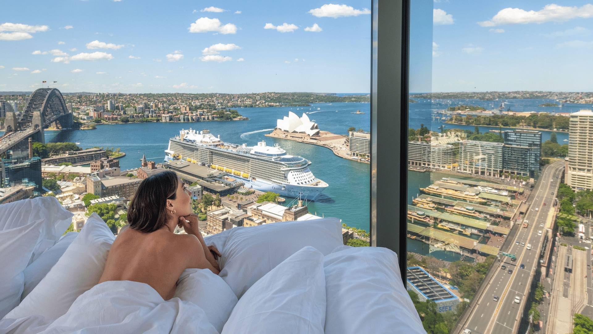 A woman in bed overlooking Sydney Harbour at the Shangri-La Sydney hotel.