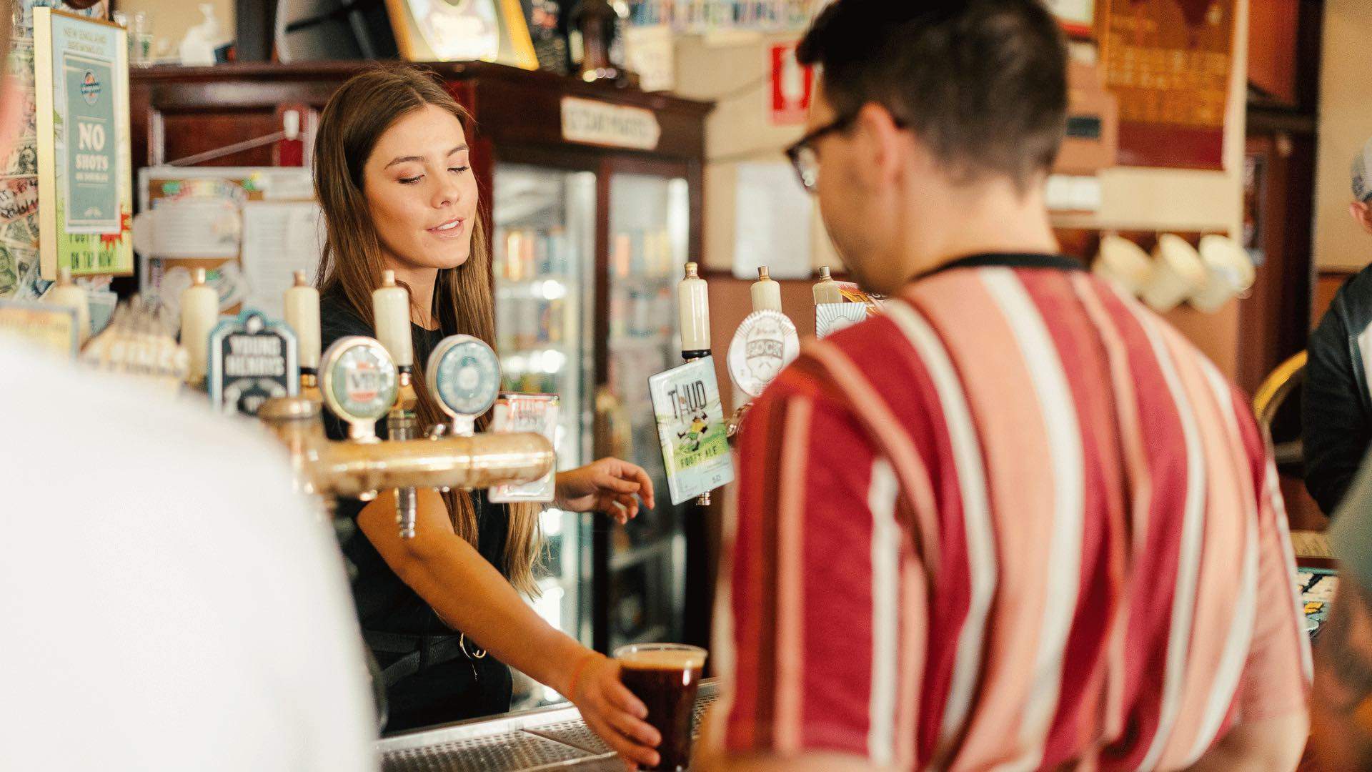 A staff member serving a person a beer at the bar.