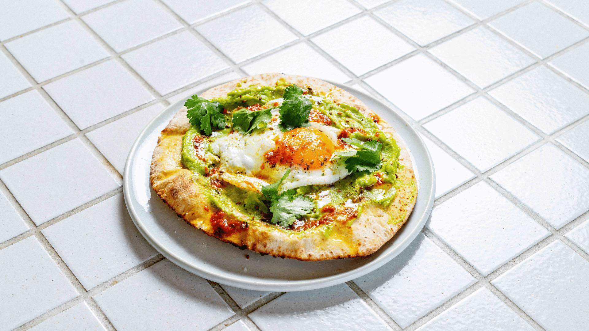 A photo of flatbread topped with avocado and a fried egg.