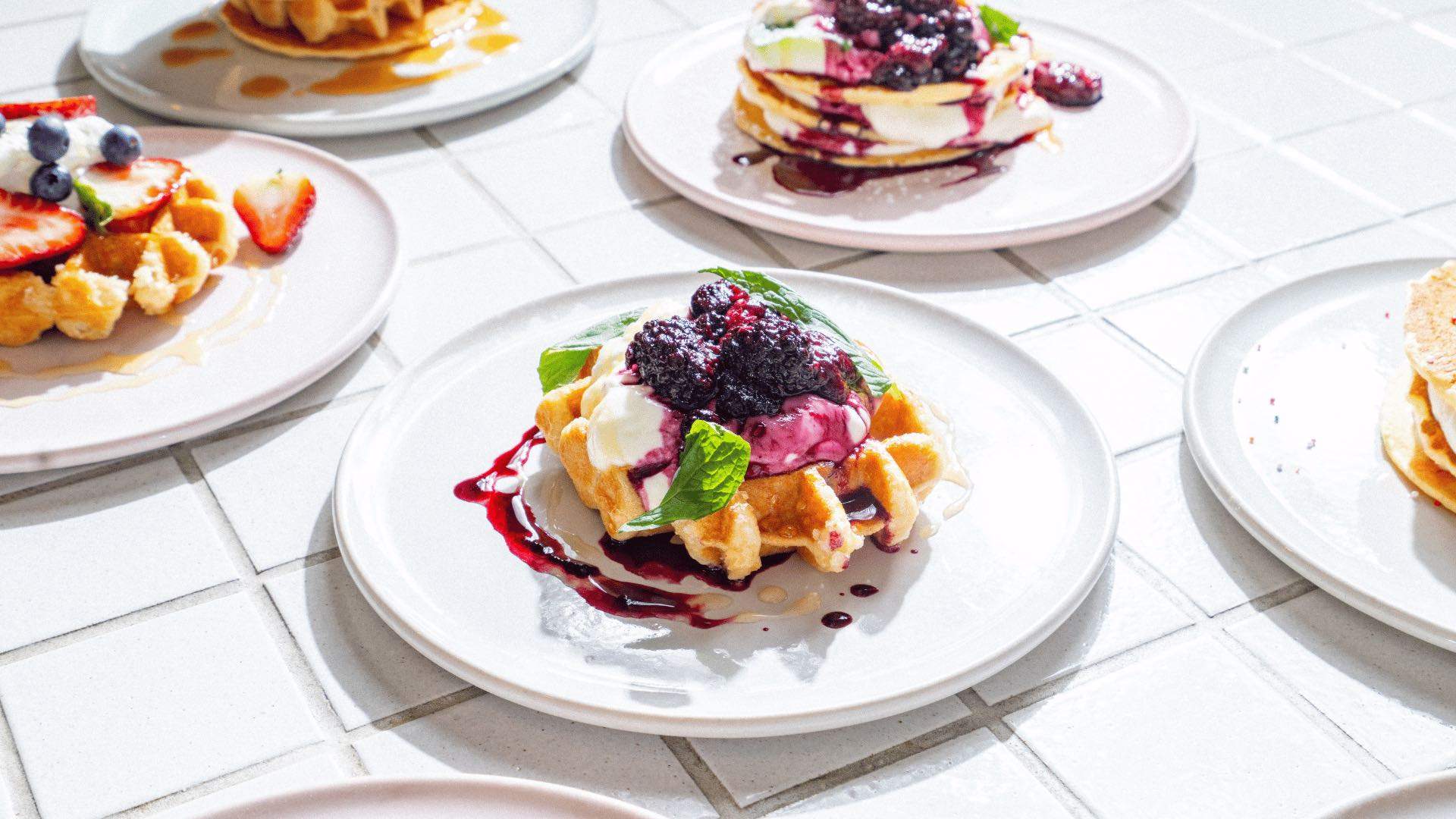 A waffle with whipped cream and berries surrounded by other pancakes and waffles.