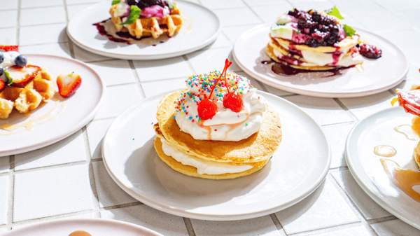 A pancake with whipped cream and cherries surrounded by other pancakes and waffles.