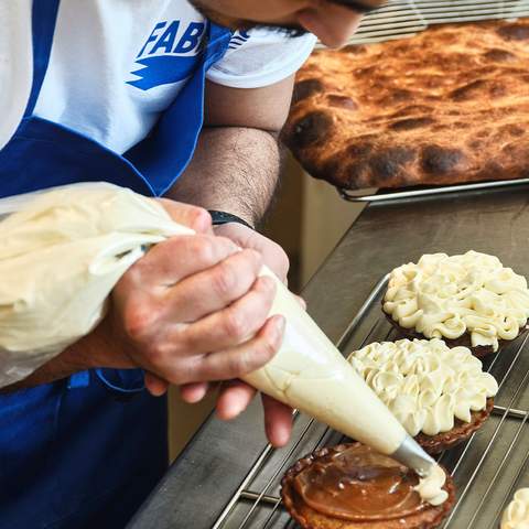 A baker piping banoffee cream onto a tart at Fabbrica Bread Shop, Rozelle