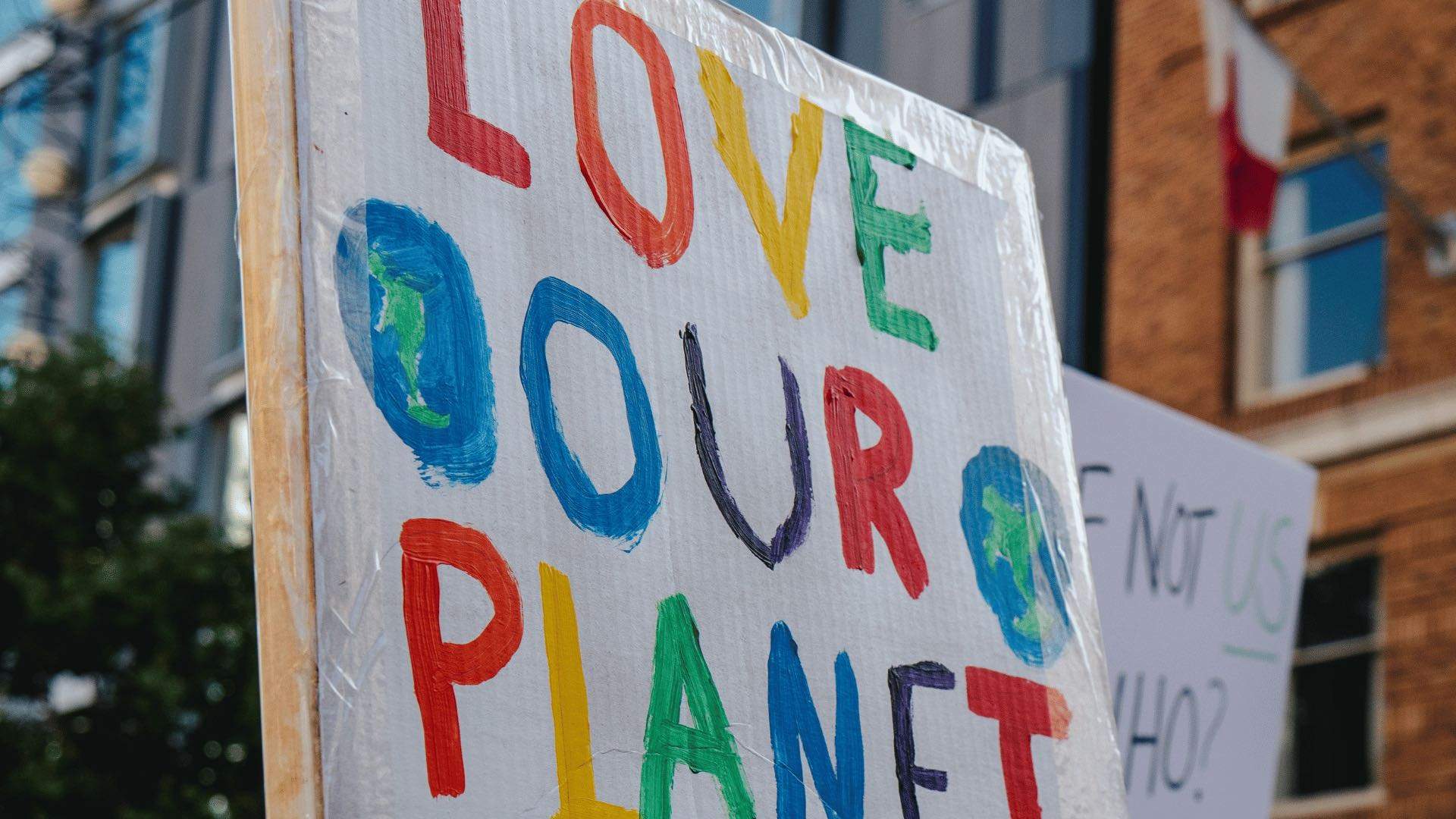 A person holding up a protest sign that reads "Love out planet".