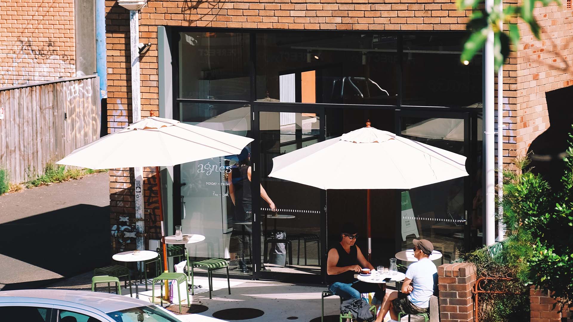 People sitting under large white umbrellas outside of the red brick cafe Agnes