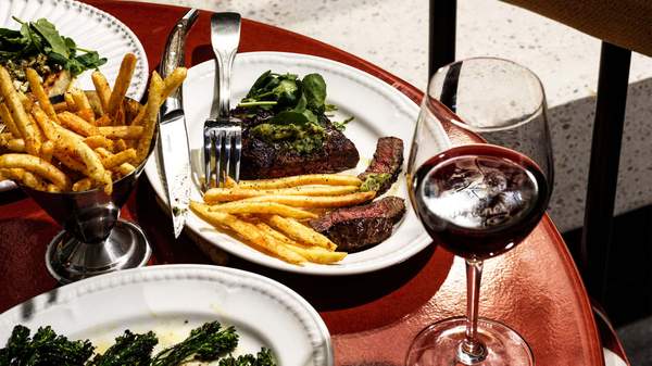 A late of steak frites on a deep red table with a glass of wine
