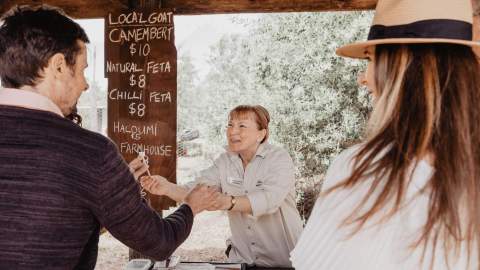 A woman greeting a couple at her cheese stand.