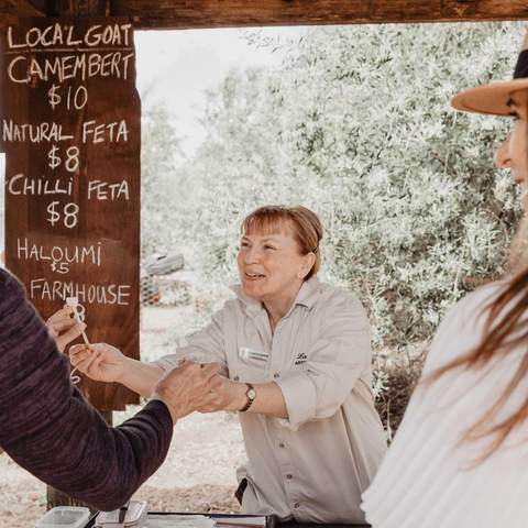 A woman greeting a couple at her cheese stand.