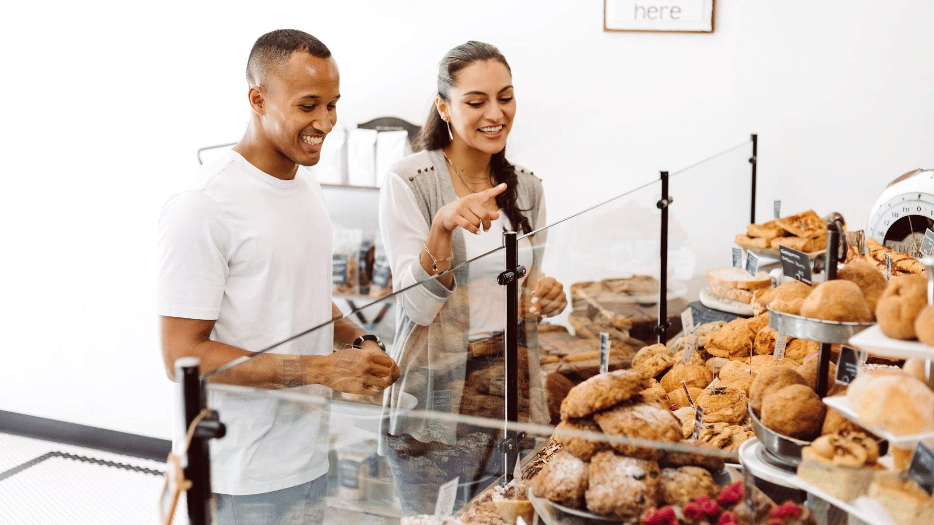 A couple pointing at baked goods in a bakery.