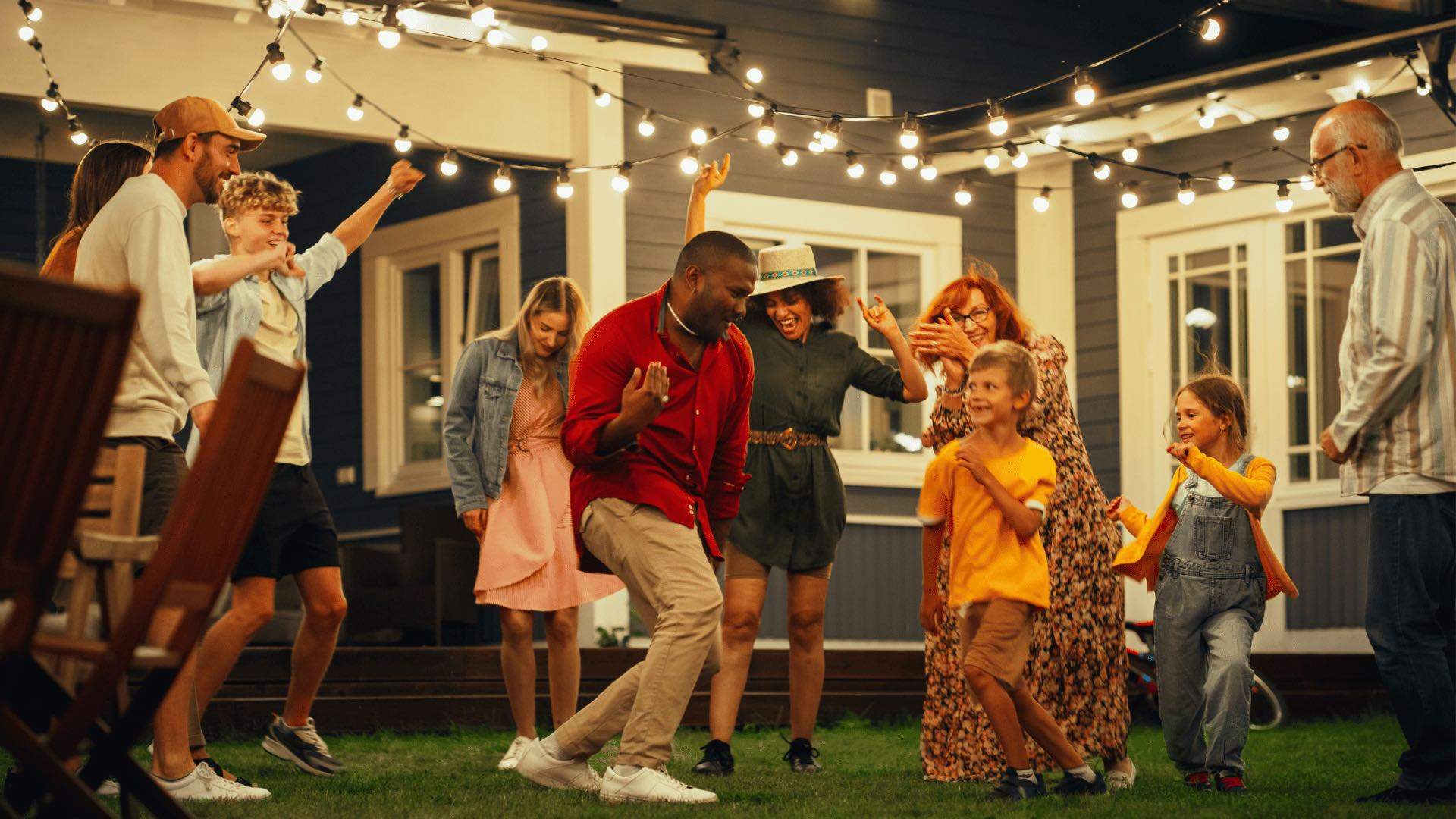 A group of people dancing under fairy lights in the backyard.