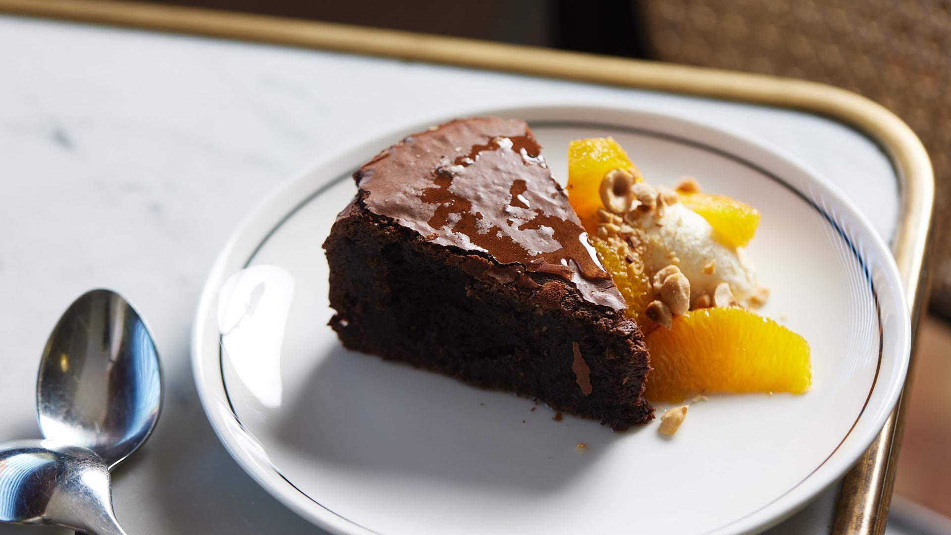 A glistening chocolate hazelnut cake with a side of nuts, cream and mandarin at The Erko.