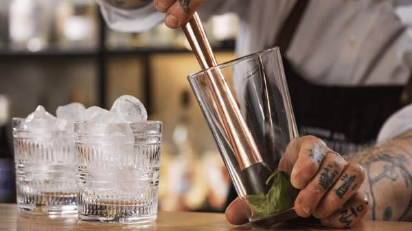 A bartender muddling mint in a glass.